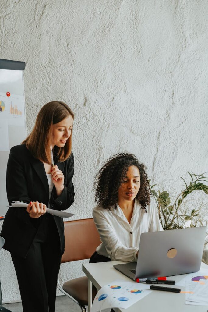 Two businesswomen sharing ideas on a project, working together on a laptop in a modern office setting. Employee Insights That Drive Business Results